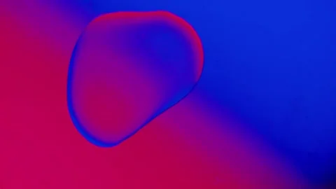 A drop spreads over the surface on a blue-red gradient background. Vídeo Stock 303058762