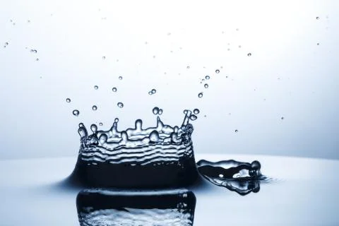 Drop of water falling down in the water Stock Photos