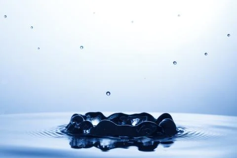 Drop of water falling down in the water Stock Photos