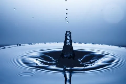 Drop of water falling down in the water Stock Photos