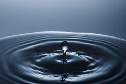 Drop of water falling down in the water Stock Photos