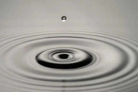 A drop of water is falling into a large circular puddle 写真素材