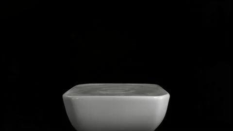 A drop of water falls into a container of water. Close-up against a black Vidéo 147329609
