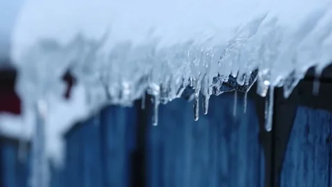 A drop of water falls from an icicle on a blue background. Close up. Spring. Ice Stock Footage 231794732