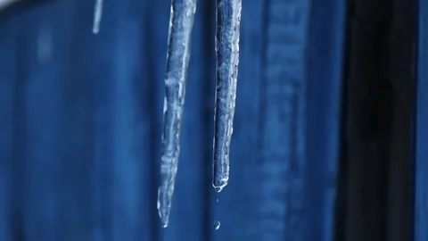 A drop of water falls from an icicle on a blue background. Close up. Spring. Ice Stock Footage 231794845