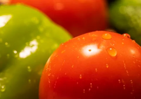 A drop of water flows down the red fresh tomato. Macro shot. Green pepper in the Stock Photos