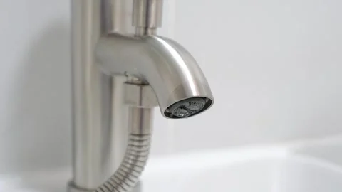 Drop of water flows from a tap in a bathroom on light background. Stock Footage 313574822