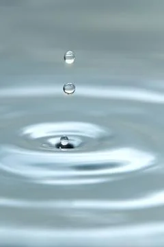 A drop of water hovering in the air before hitting a water surface, which will Stock Photos