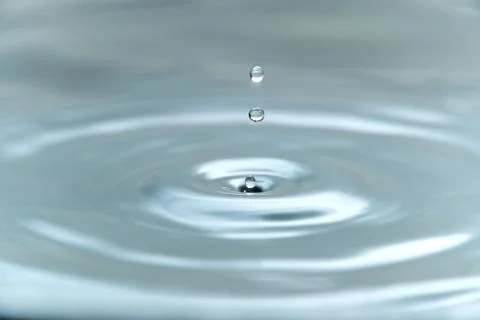 A drop of water hovering in the air before hitting a water surface, which will Stock Photos