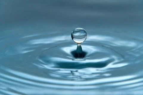 A drop of water hovering in the air before hitting a water surface, which will Stock Photos