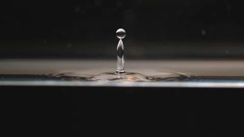 Drop of water splashes back upwards from puddle Stock Photos