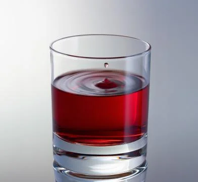 Drop of wine fly up above the surface in glass. Red wine glass close up Stock Photos