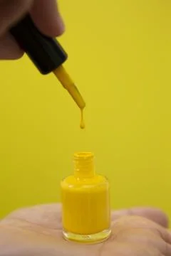 Drop of yellow nail polish falling on the can while being held by a woman's.. Stock Photos