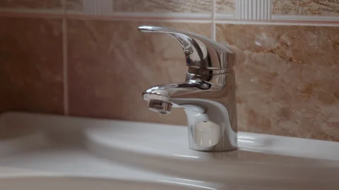 Droplets of crystal-clear water fall metal faucet smooth ceramic basin below Stock Footage 274652967