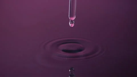 Droplets fall from a pipette onto a violet water surface, spreading ripples.. Video stock 301351174
