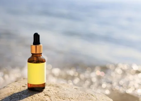 Dropper bottle with blurred beach backdrop. Natural cosmetic or medicine conc Stock Photos