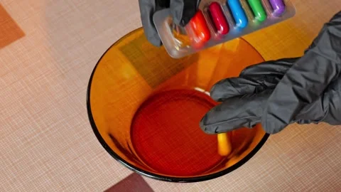 Dropping egg dye capsule from blister into glass bowl slow motion 库存影片 332629256