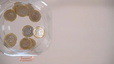 Dropping Pound Coins into Jar Stock Footage 123807965