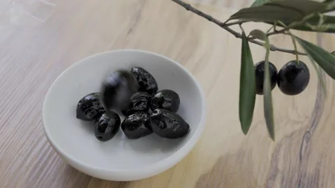 Dropping ripe black olives into white bowl wooden table 4k Stock Footage 340522365