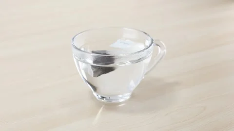Dropping a Tea Bag into Clear Glass Cup of Hot Water Stock Footage 346664639