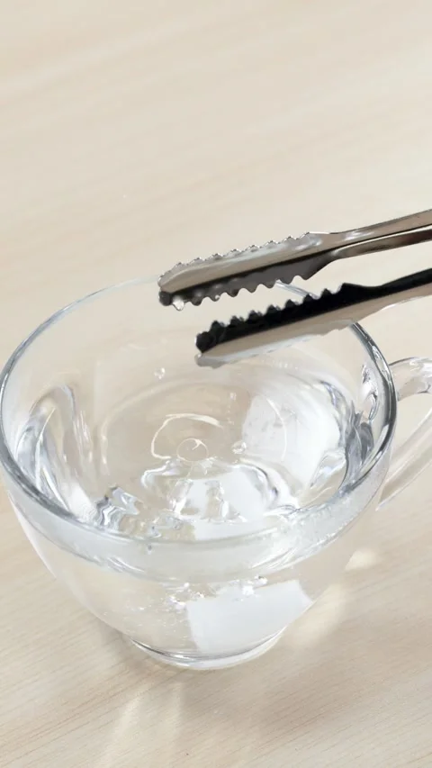 Dropping a White Sugar Cube into a Glass Cup of Water Stockbeeldmateriaal 345779293