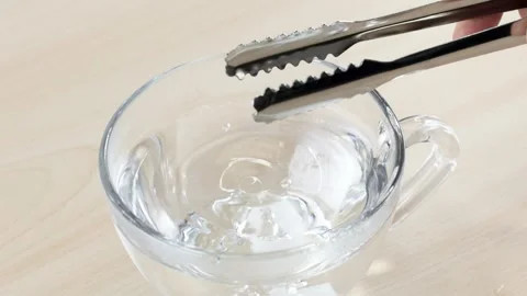 Dropping White Sugar Cube into Glass Cup of Water with Tongs Stock Footage 346121451