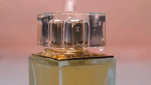 Drops and splashes of water fall on a square bottle of golden perfume Stock Footage 153001664