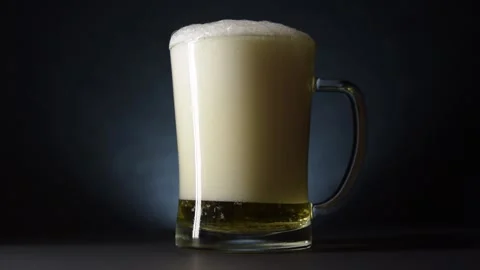 Drops of beer run down the sides of an overflowing beer mug. Slow motion and Video stock 130937698