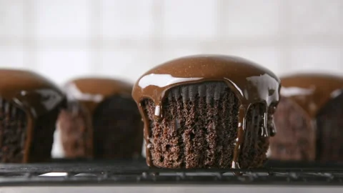 Drops of chocolate sauce slowly drip down chocolate cupcakes on a blurred white Stock Footage 219830080