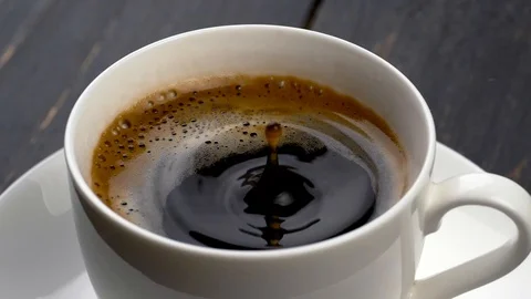 Drops of coffee are falling into espresso cup. Black wooden background. Stock Footage 86010301