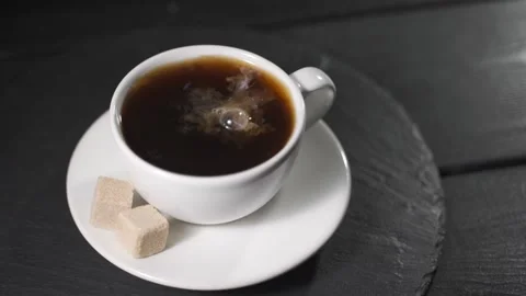 Drops of cream drip into the coffee cup. Fragrant coffee with sugar cubes on a Stock Footage 154642278