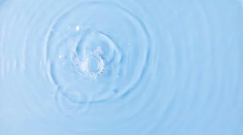 Drops fall down into clear fresh water on light blue background view from above Foto stock