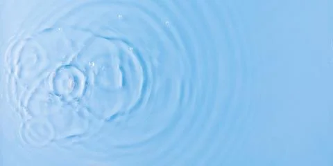 Drops fall down into clear fresh water on light blue background view from above Foto stock