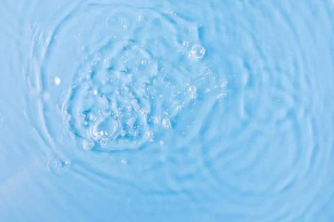 Drops fall down into clear fresh water on light blue background view from above Foto stock