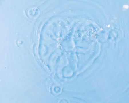 Drops fall down into clear fresh water on light blue background view from above Stock-Fotos