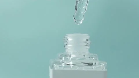 Drops fall from the dropper into a small glass bottle on a light blue background Stock Footage 205581384
