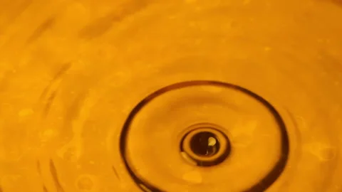 Drops falling into a pool of gold liquid creating ripples in slow motion Stock Footage 148491519