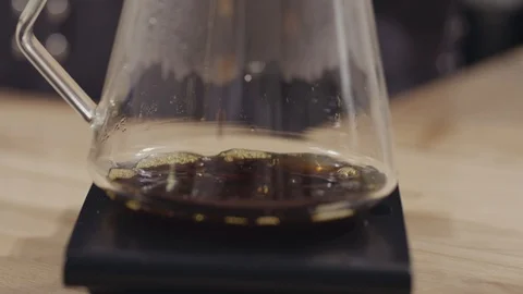Drops of freshly made coffee drip into a glass jar on a wooden table. Full HD Stock Footage 129638889