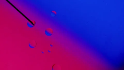Drops from a medical needle fall on a red-blue gradient background. 스톡 동영상 303059459