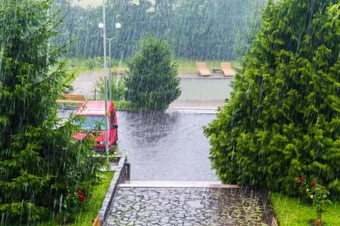 Drops of very heavy rainfall fall on asphalt and trees near the hotel complex Stock Photos