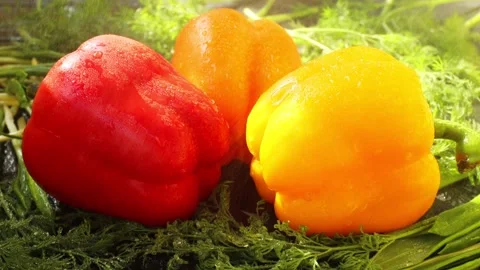 Drops of water fall from above on three sweet peppers, red, orange, yellow Stock Footage 239844865