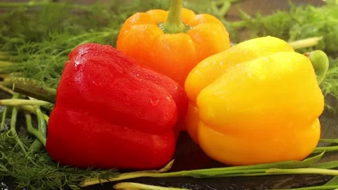 Drops of water fall from above on three sweet peppers, red, orange, yellow Stock Footage 239844984