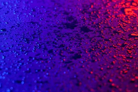 Drops of water on a textural surface in neon light. Reflection of red-blue li Stock Photos