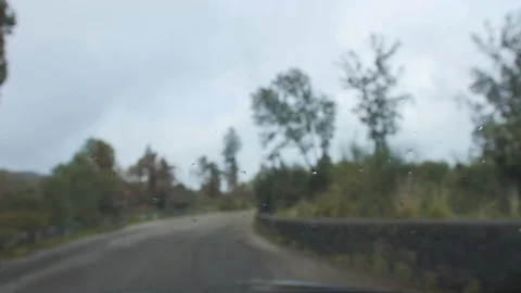Drops on windshield and blurred view of countryside road from a car in cloudy Stock Footage 100743417