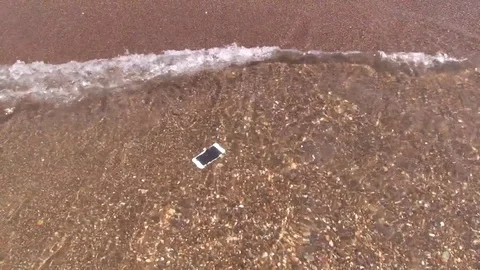 Drown smartphone floats on bottom in waves of sea surf sandy beach. Stock Footage 79161638