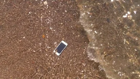 Drown smartphone floats on bottom in waves of sea surf sandy beach. Slow Motion Stock Footage 79193969