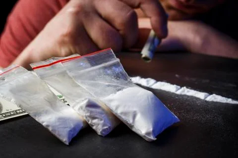 Drug addict man using narcotics, sniffing cocaine lines white powder with rol Stock Photos