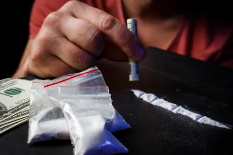Drug addict man using narcotics, sniffing cocaine lines white powder with rol Stock Photos