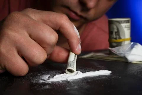 Drug addict man using narcotics, sniffing cocaine lines white powder with rol Stock Photos