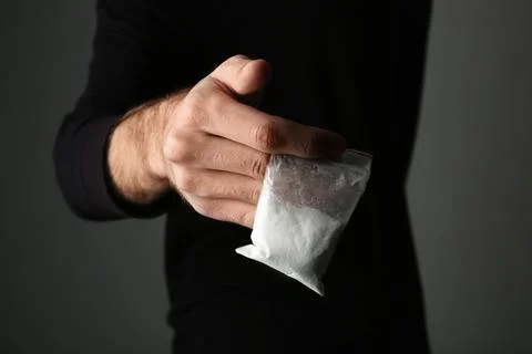Drug dealer holding bag with cocaine on dark background, closeup Stock Photos